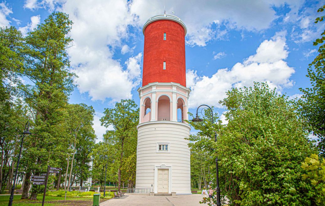 Ķemeri water tower against a blue sky background among green leafy trees